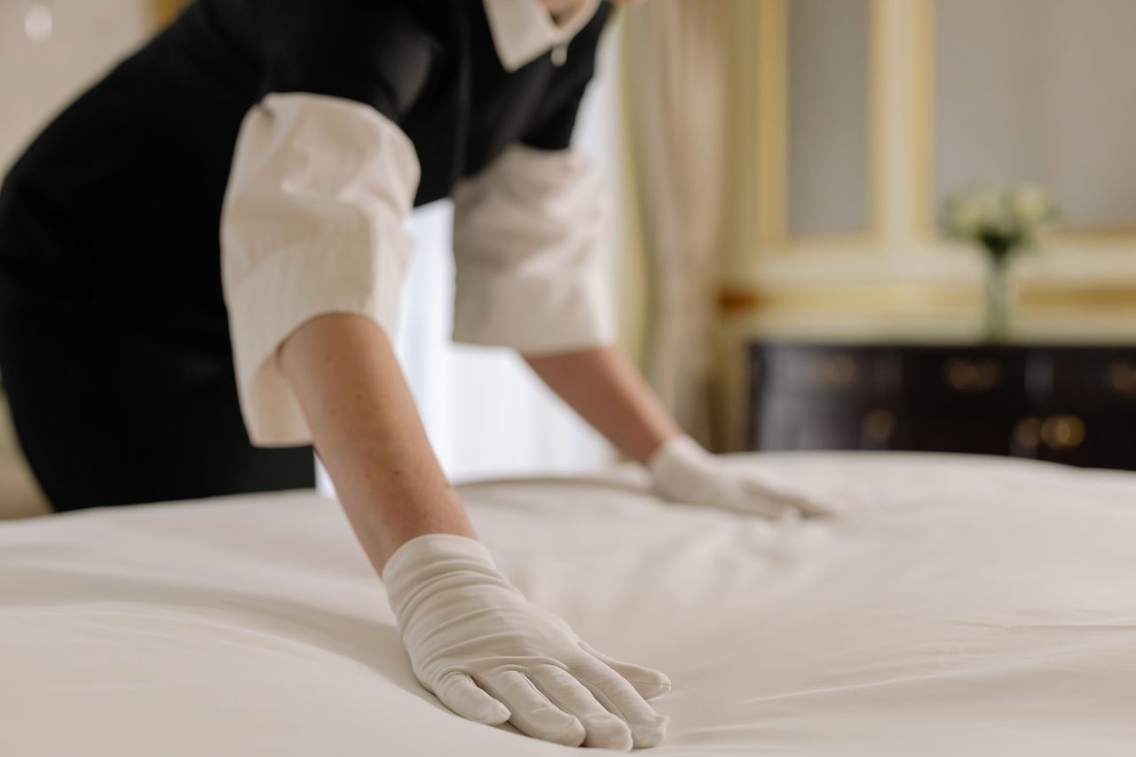 services-04 A housekeeper straightening the bed linens in a well-appointed hotel room.